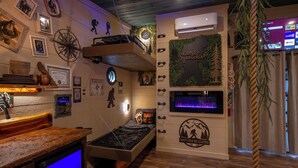 Ein Zimmer mit einem Etagenbett, einem kleinen Schreibtisch mit Computer, einem Wand-Fernseher und verschiedenen Dekorationen, darunter ein Kompass, gerahmte Fotos und ein Schild mit der Aufschrift 'Don't Stop Be-Leafing'.