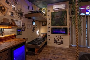 Ein Zimmer mit einem Etagenbett, einem kleinen Schreibtisch mit Computer, einem Wand-Fernseher und verschiedenen Dekorationen, darunter ein Kompass, gerahmte Fotos und ein Schild mit der Aufschrift 'Don't Stop Be-Leafing'.