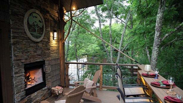 A wooden deck with a stone fireplace, wooden chairs, and a dining table set for a meal. - 63-OWL ALWAYS LOVE YOU (Sevierville)