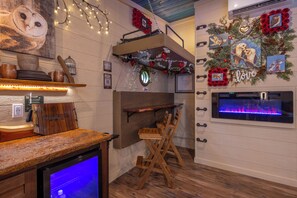 Ein gemütliches Zimmer mit einer Holzbank, einem kleinen Tisch, einem Kamin und Wanddekorationen, darunter Bilder von Herz und Eule.