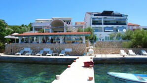 Ein Hotel direkt am Wasser mit Poolbereich, Liegestühlen und Bootsanleger.