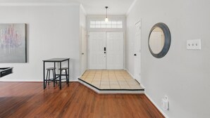 A spacious room with hardwood flooring, a white door, a small table with stools, a ceiling light, and a wall-mounted mirror. - Modern 4BR Pool Home | Flower Mound ISD (Flower Mound)