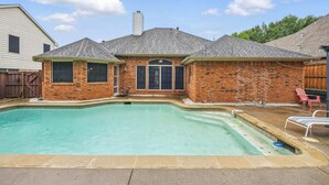 A backyard with a swimming pool, a brick house, and a wooden fence. - Modern 4BR Pool Home | Flower Mound ISD (Flower Mound)