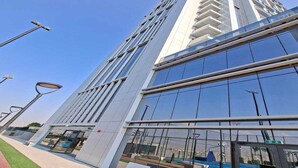 A modern high-rise building with a glass facade, a pedestrian walkway, and a bench area. - Luxury Living at Cloud Tower JVT with  (Dubai)