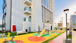 A modern building with a playground area featuring slides and swings, surrounded by a well-maintained lawn and a paved walkway. - Luxury Living at Cloud Tower JVT with  (Dubai)