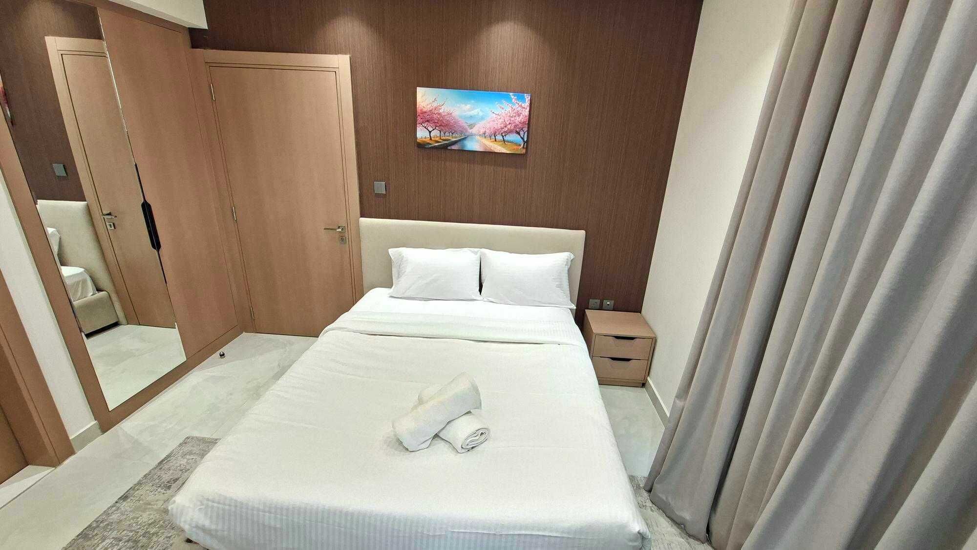 A hotel room with a bed, a nightstand, a painting on the wall, and a door.