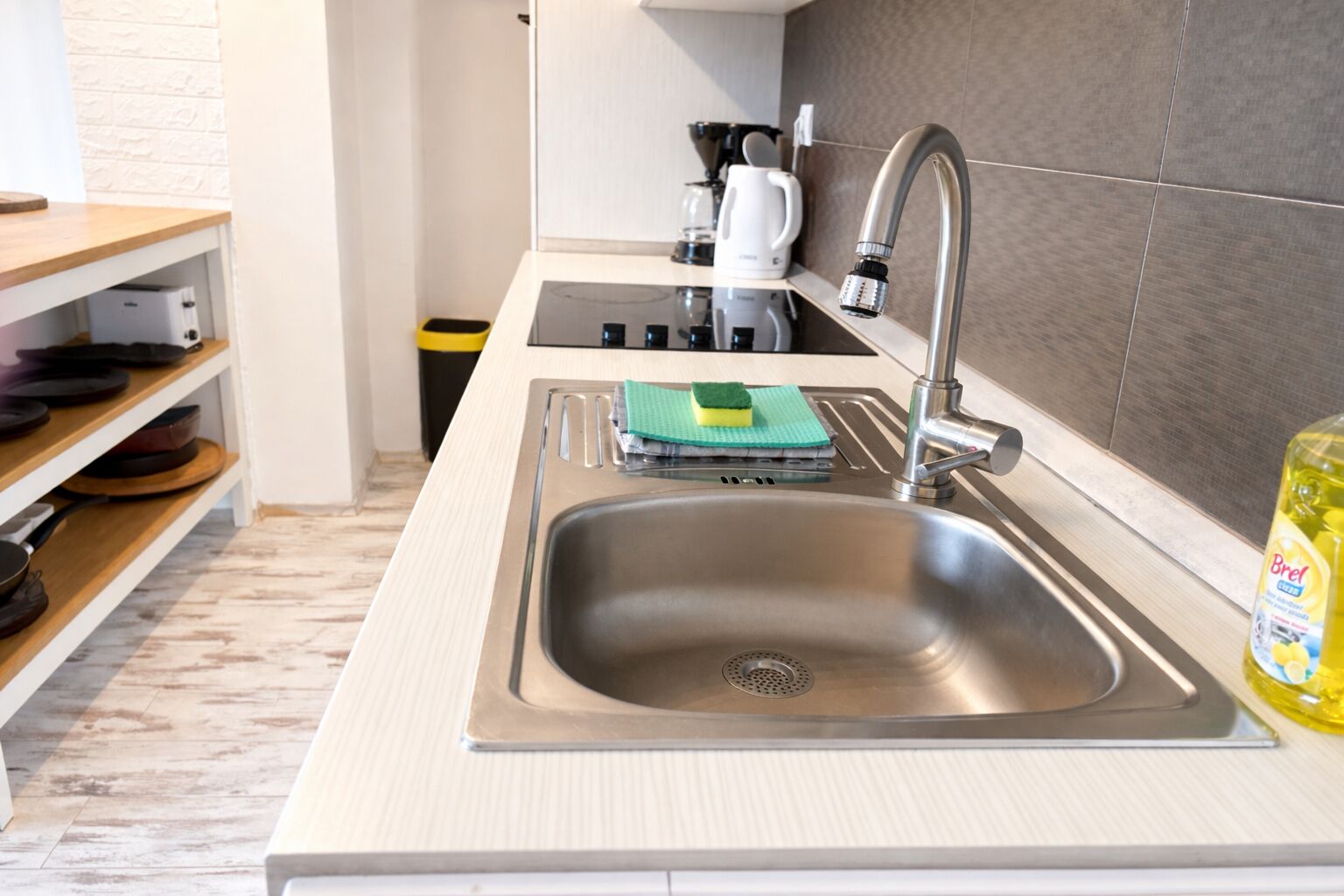 A modern kitchen with a stainless steel sink, a coffee maker, and a bottle of dish soap.