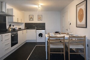A compact kitchen with a washing machine, a stove, and a dining area set for two. - Deluxe Double Bed Flat with Free Parking (Salford)