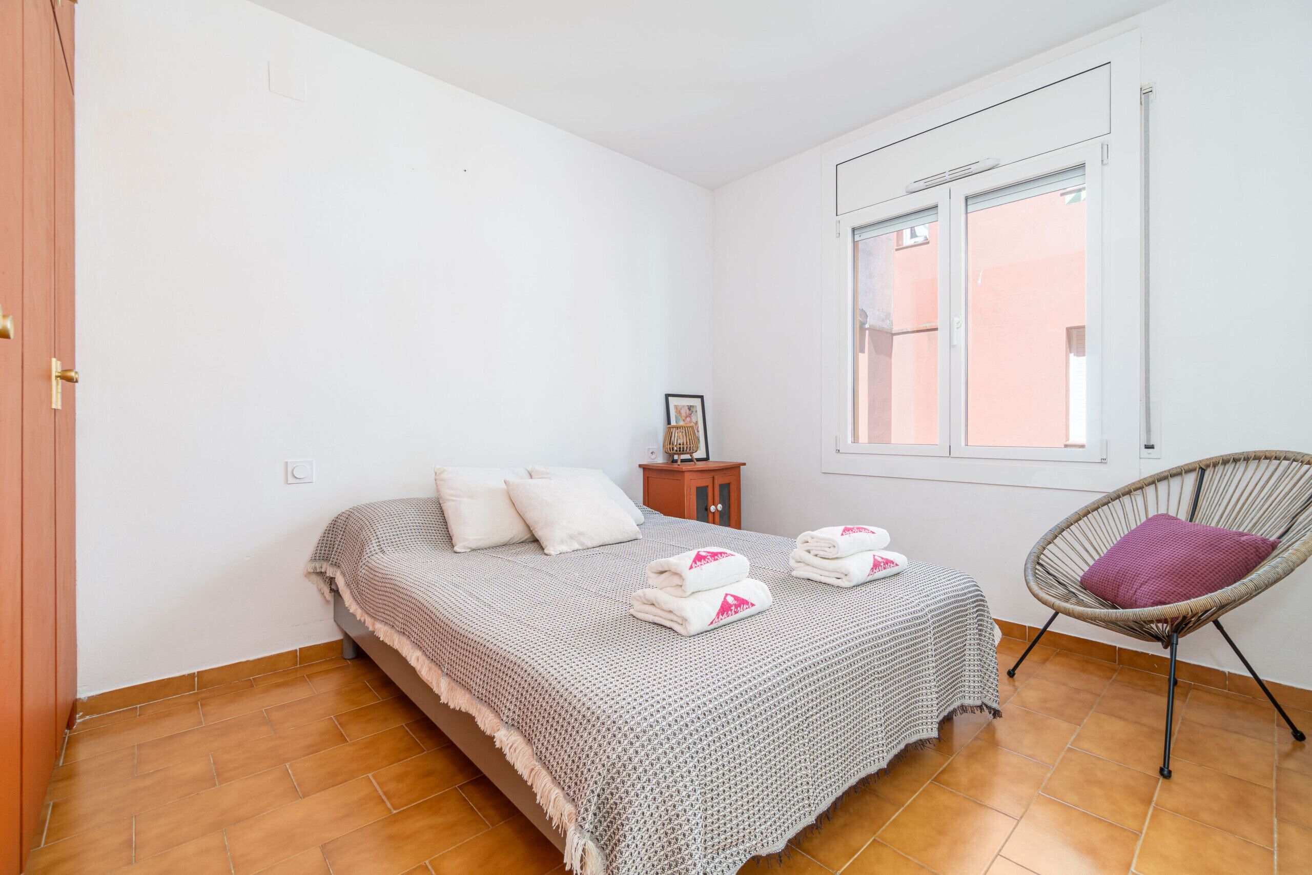 Een slaapkamer met een bed, een stoel, een raam en een klein tafeltje.