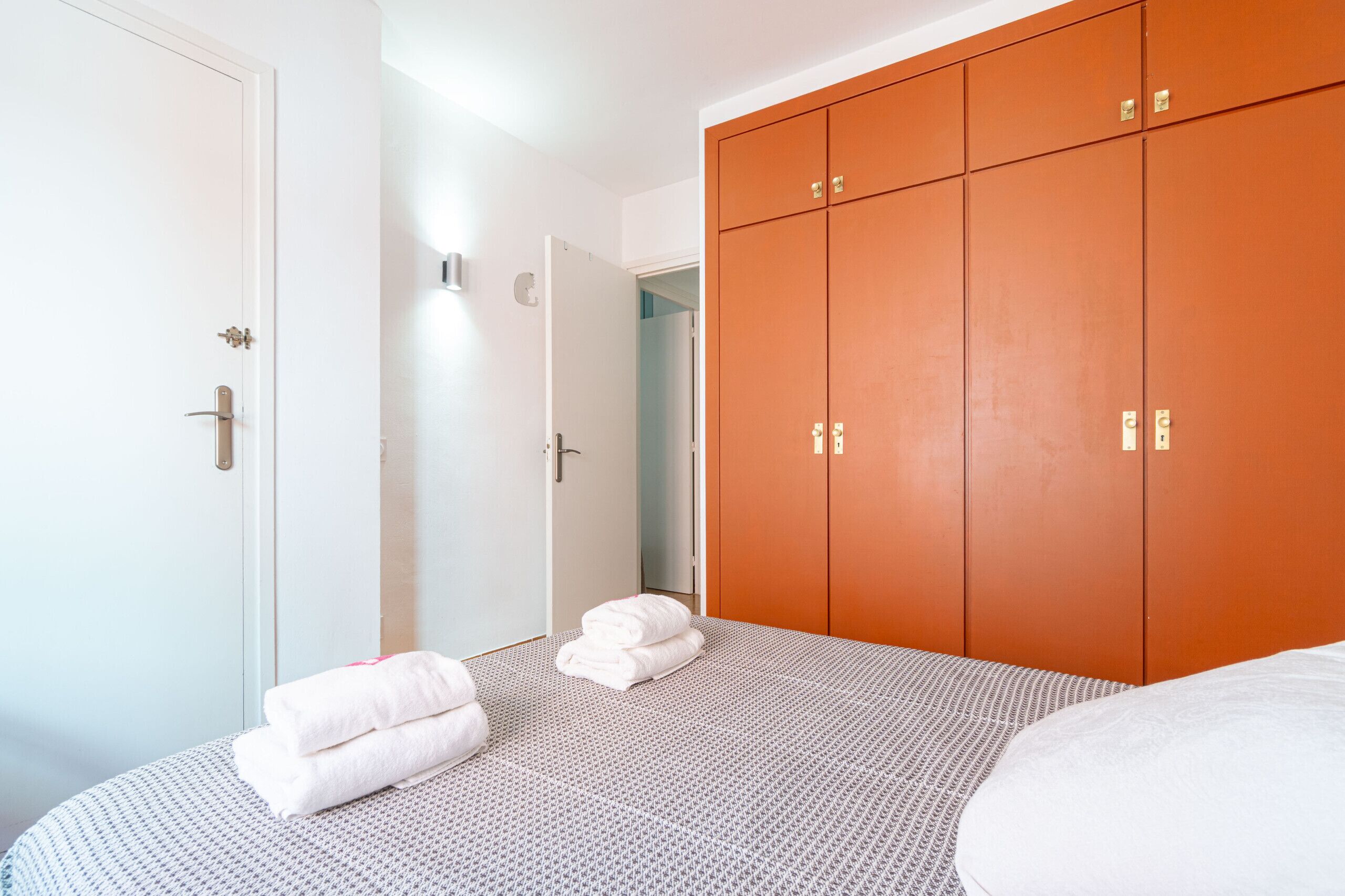 A hotel room with a bed, a wardrobe, and a door leading to another room.