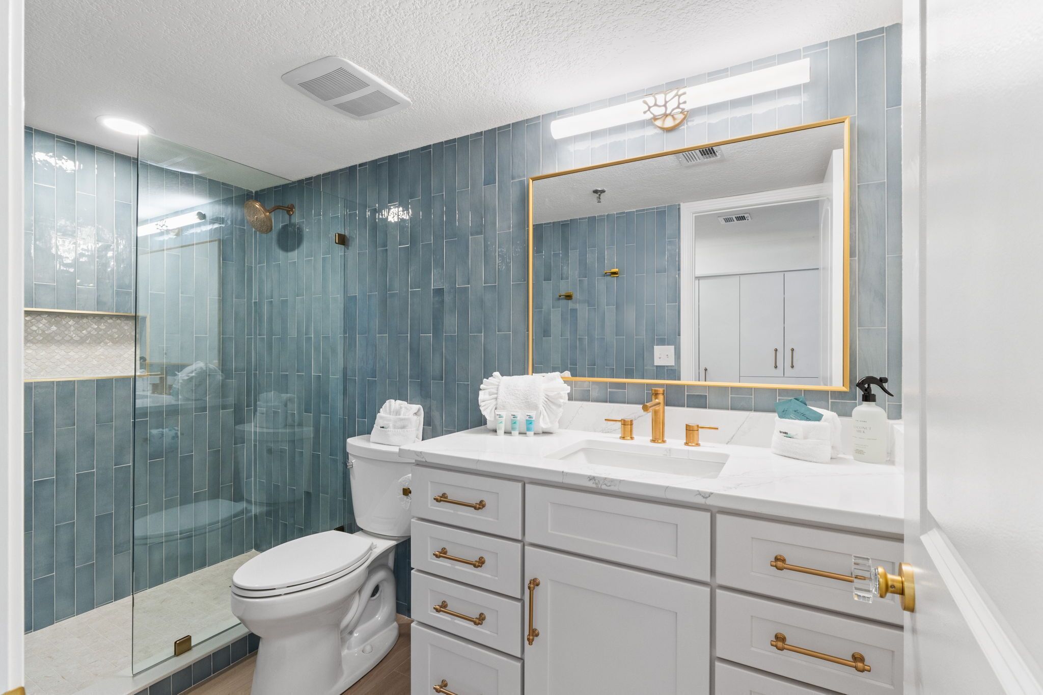 A modern bathroom with a glass shower enclosure, white vanity with gold handles, and a large mirror with a gold frame.
