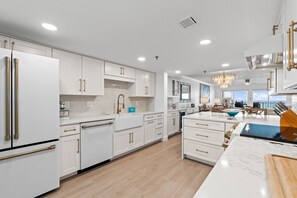 A modern kitchen with white cabinetry, a large island, and a dining area with a view. - SD 405: Emerald Beach Hide Away (Ft Walton Beach)