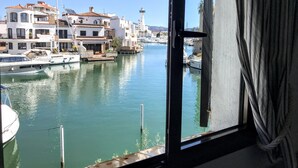 Un puerto deportivo con barcos amarrados, un faro al fondo y edificios con balcones.