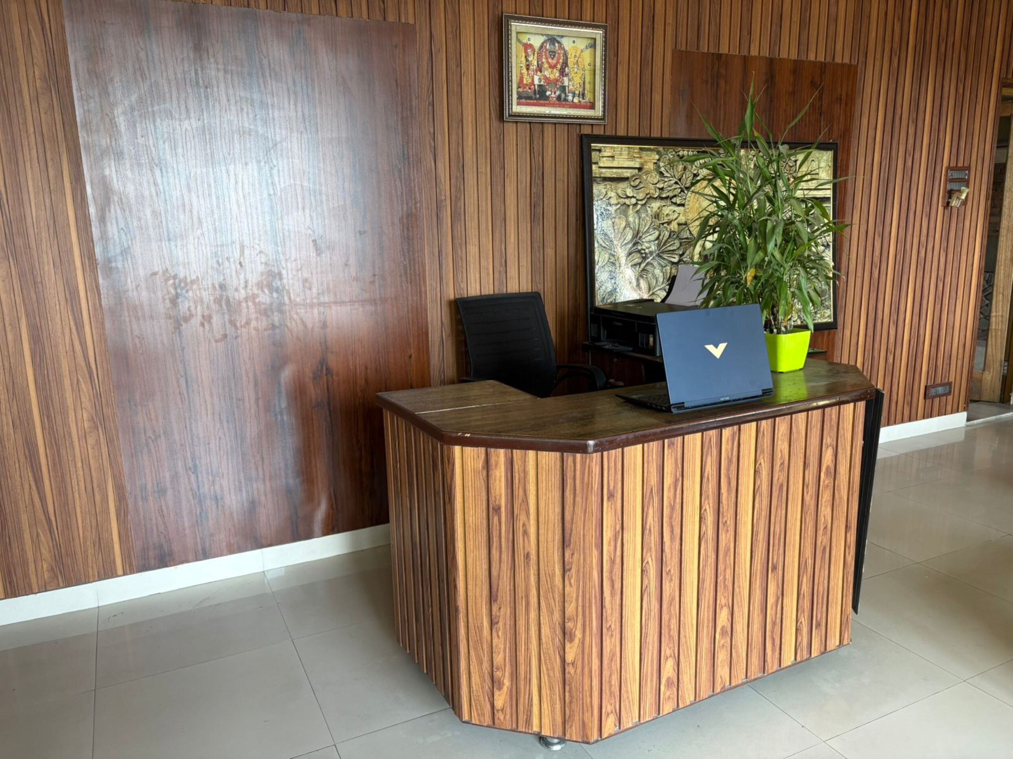 A reception desk with a laptop, a potted plant, and a framed picture on the wall.