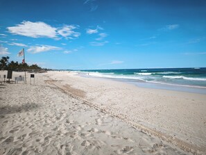 En strand med klar himmel, sandstrand och några få flaggor.