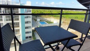 A balcony with two black wicker tables and chairs, overlooking a swimming pool and a green landscape. - Apartment Brisa Del Mar Punta Cana (Punta Cana)