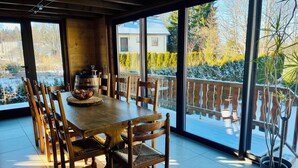 A dining area with a wooden table and chairs, a potted plant, and a view of a snowy deck outside. - Mountain vacation home 10 people village center (Prémanon)