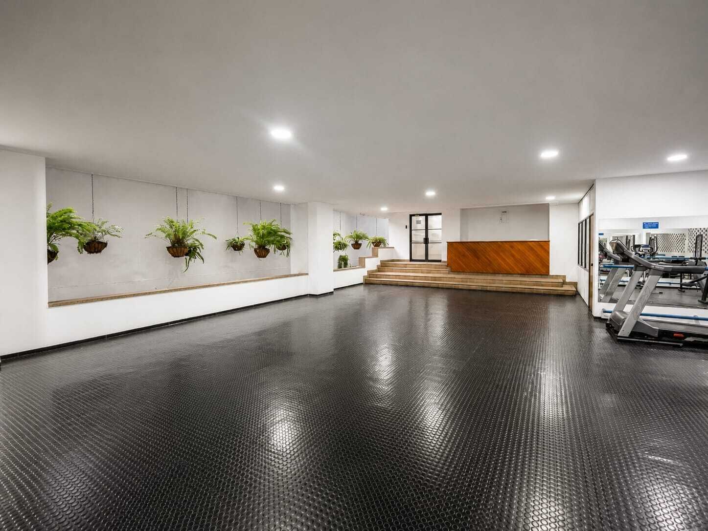 Amplio espacio interior con mostrador de recepción, una escalera y equipo de ejercicio.