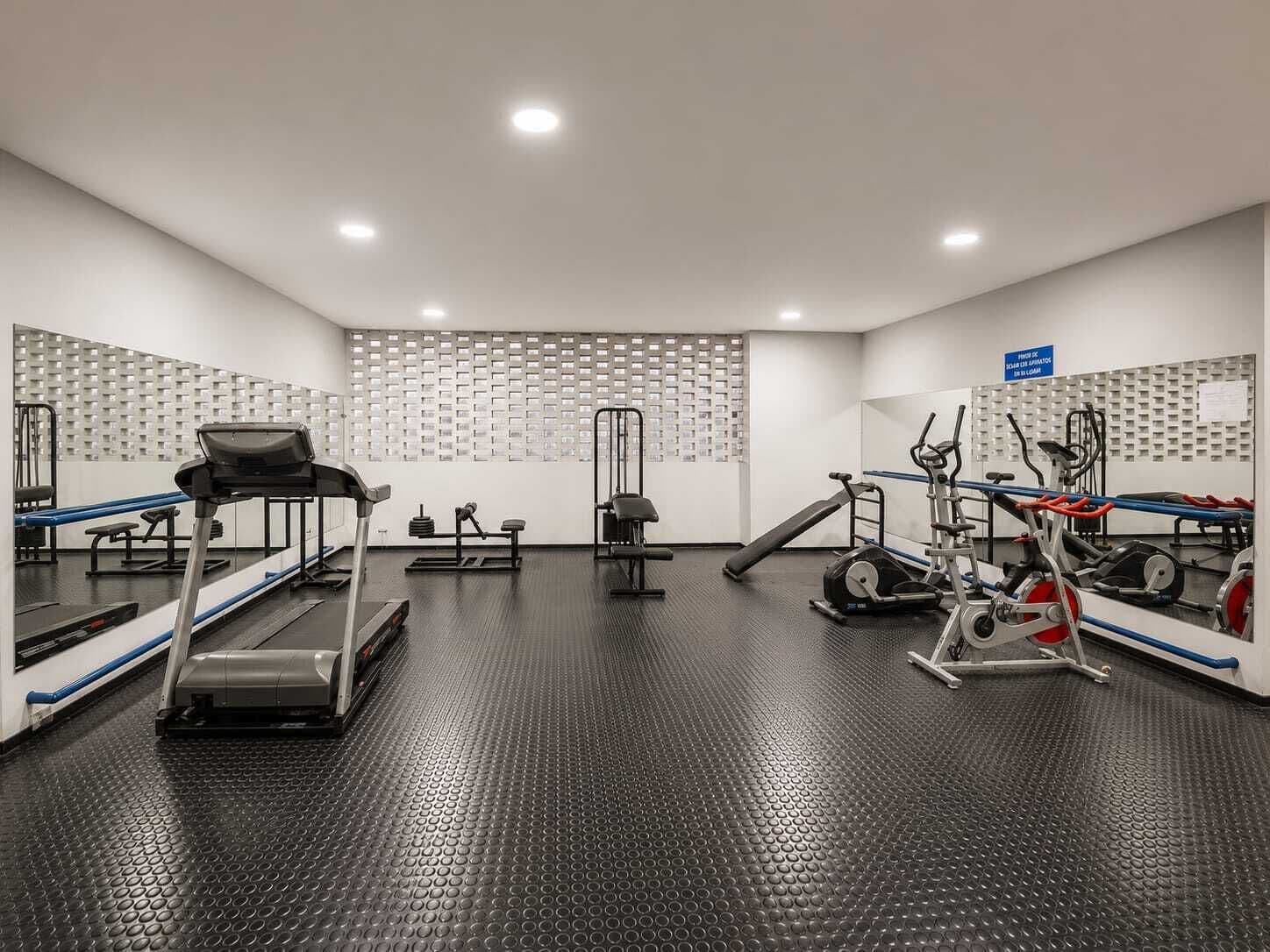 A gym with treadmills, weight machines, and a mirrored wall.