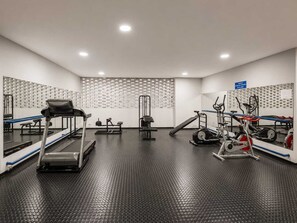 Une salle de sport équipée de tapis de course, d’appareils de musculation et d’un mur recouvert de miroirs.