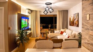 A modern living room with a flat-screen TV, a sofa set, a dining table, and a decorative ceiling light. - Luxury Apartment in Cali's Zona Rosa—Terrazas de Granada (Cali)