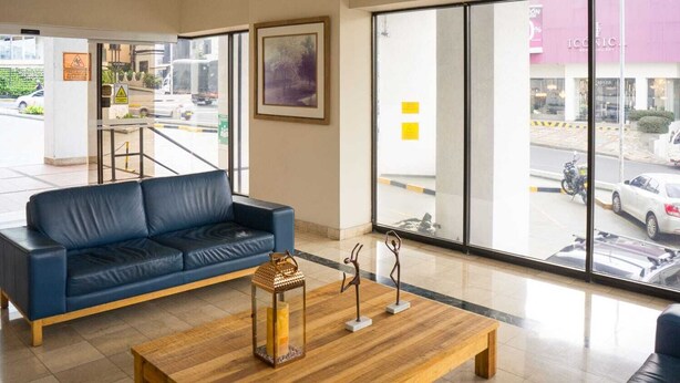 A modern lobby with a blue leather sofa, a wooden coffee table, and a large window offering a view of the street. - Luxury Apartment in Cali's Zona Rosa—Terrazas de Granada (Cali)