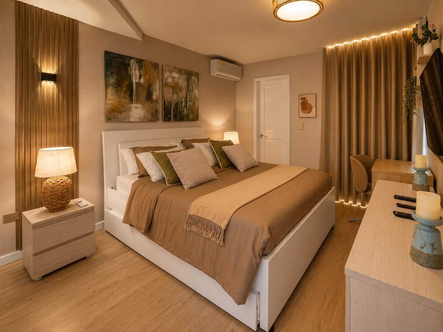 A modern bedroom with a large bed, bedside lamps, a desk with a mirror, and a painting on the wall.