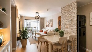 A modern living room with a sofa, dining table, and chairs, a kitchen area with a refrigerator, and a balcony with a railing. - Luxury Apartment in Cali's Zona Rosa—Terrazas de Granada (Cali)