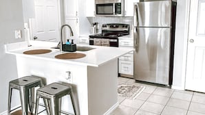 A modern kitchen with white cabinets, stainless steel appliances, and a central island with stools. - Gateway Denton (Denton)
