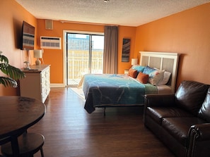 Une chambre d’hôtel avec un lit, un canapé en cuir, un bureau avec une lampe et une vue sur l’extérieur grâce à une porte coulissante.