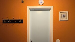 Een deur met een lichtschakelaar erboven, een kapstok links en een lijst met een afbeelding rechts.