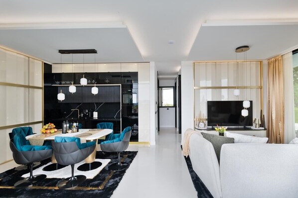 A modern living room with a sofa, a TV, and a dining area with chairs and a table.