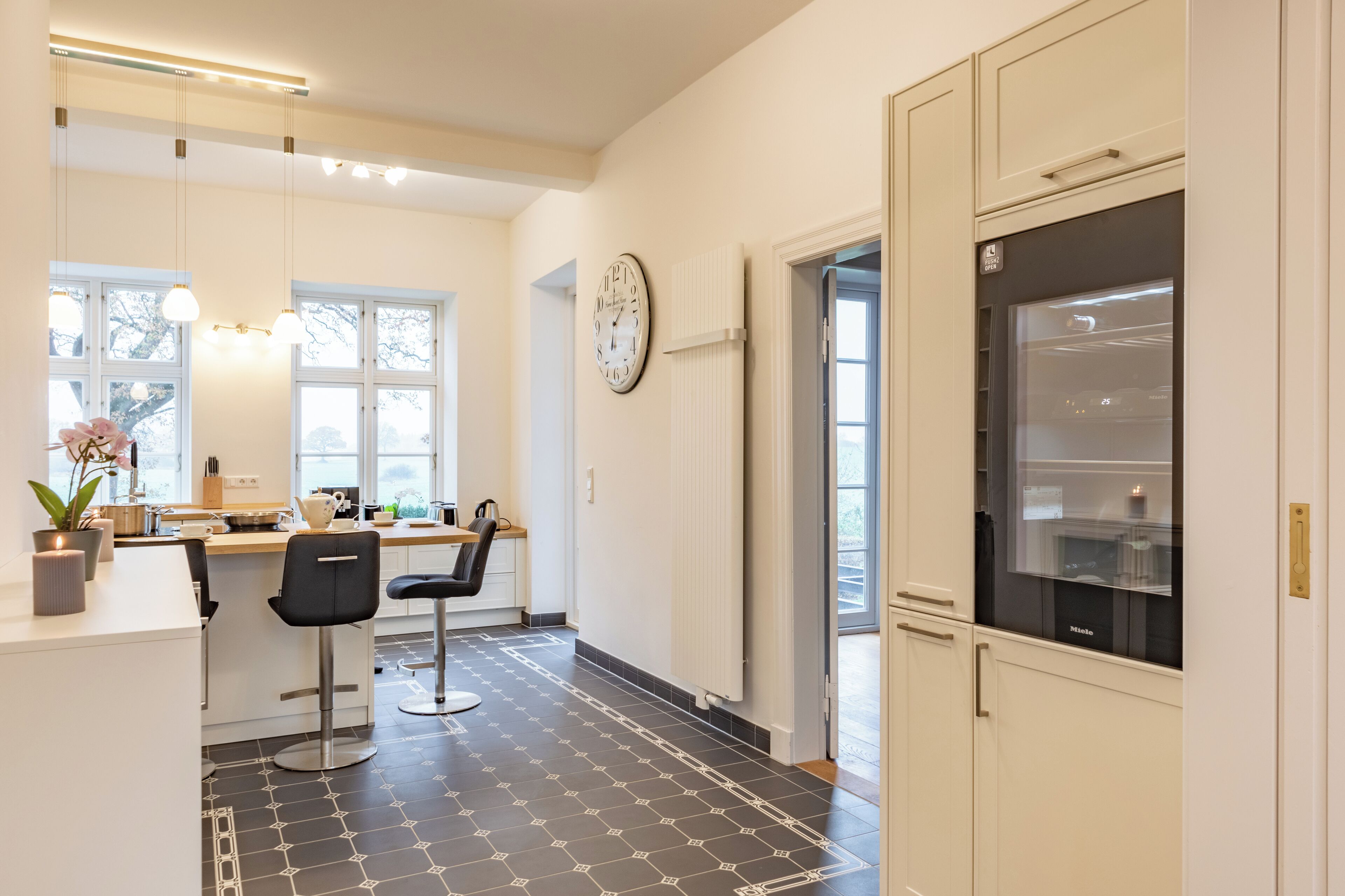 A modern kitchen with a black and white patterned floor, white cabinetry, and a large window.