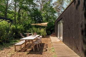 A wooden deck with a table and chairs, surrounded by dense greenery and trees.