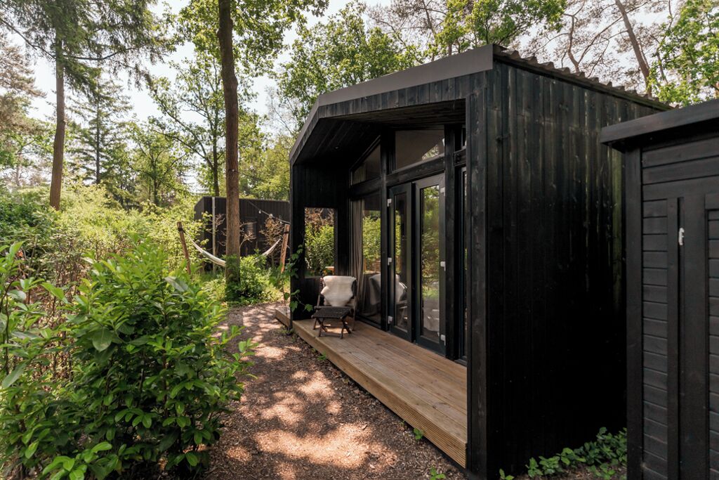 Una cabaña de madera moderna con terraza, rodeada de un bosque denso.