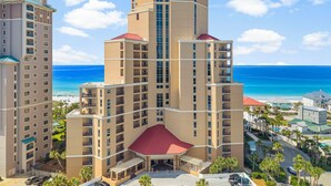 A multi-story hotel with a central courtyard and a view of the ocean. - 3BR Beachfront Resort Condo - Wraparound Balcony, Pool, Hot Tub, Tram, Beach. (Miramar Beach)