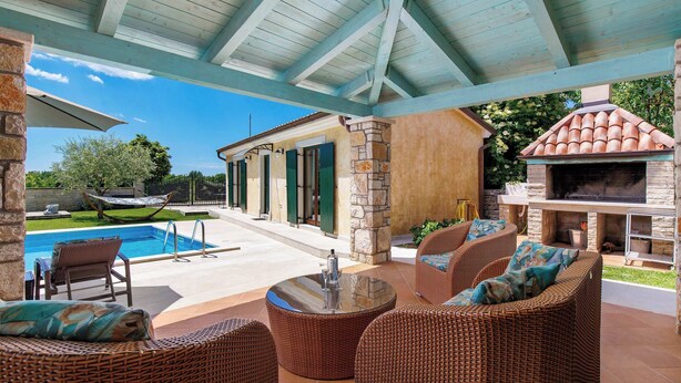 Eine überdachte Terrasse im Freien mit Korbmöbeln, einem Pool und einem Kamin aus Stein.