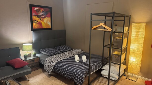 Una camera compatta con un letto a castello, un comodino con lampada, un cuscino rosso, un quadro incorniciato appeso alla parete e una lampada da terra.