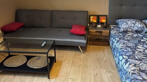 Un soggiorno moderno con un divano grigio, un tavolino in legno, una coperta a fiori blu e un quadro appeso al muro.
