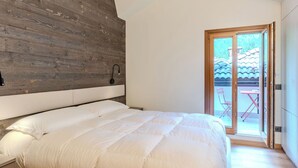 A bedroom with a wooden headboard, a bed with white bedding, a bedside lamp, and a sliding glass door leading to an outdoor area with a table and chairs.