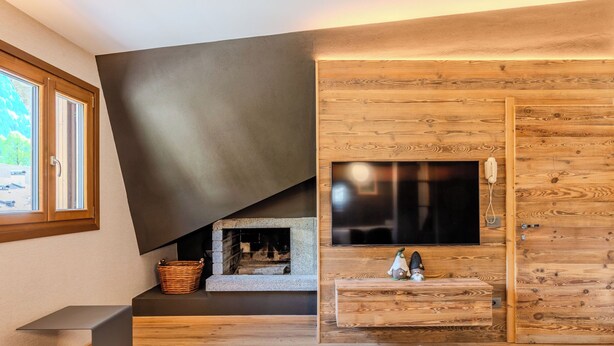 A modern bedroom with a fireplace, wooden wall paneling, a television, and a window.