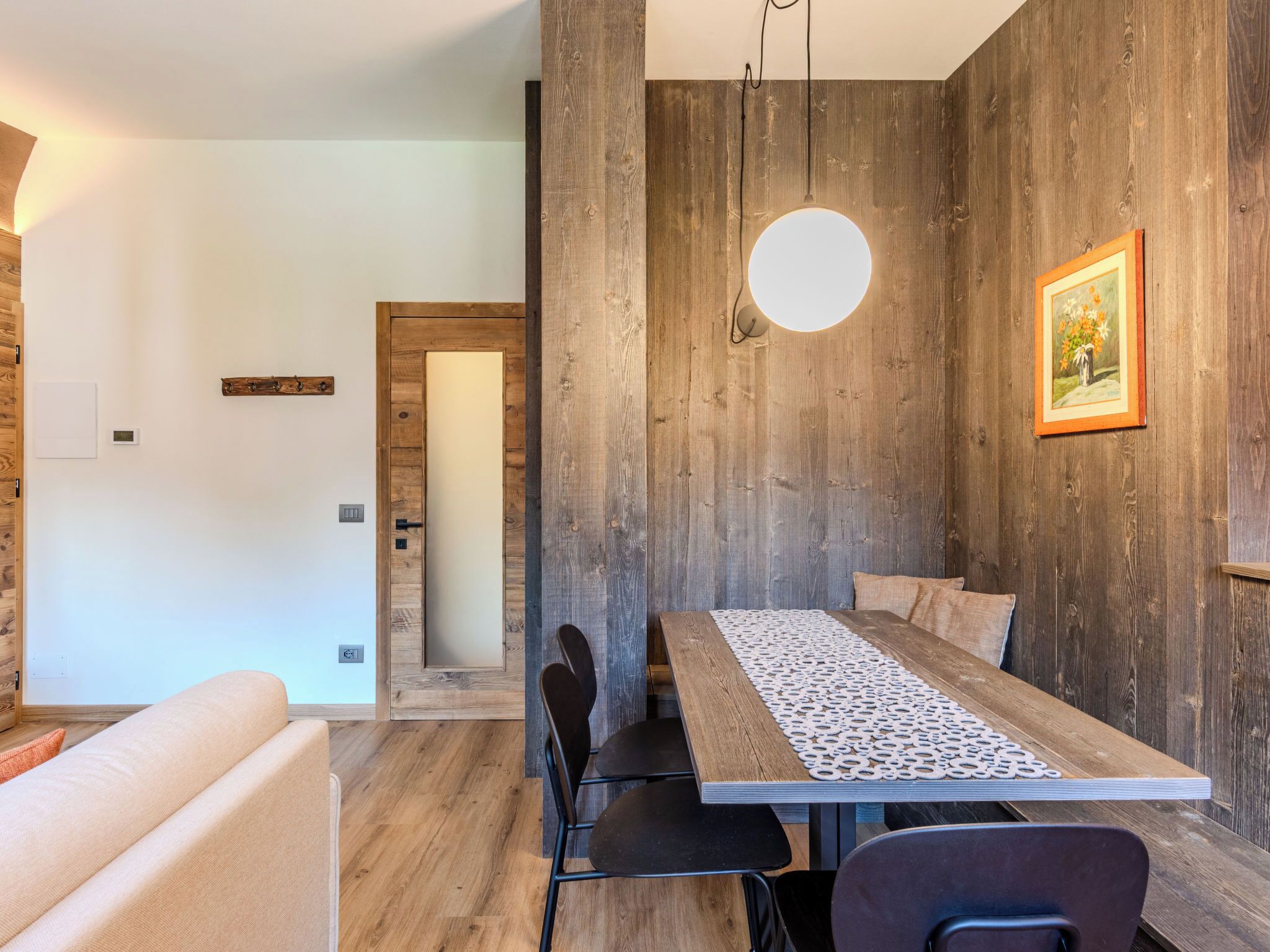 A modern dining area with a wooden wall, a round light fixture, and a framed picture.