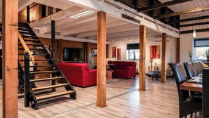 A spacious loft-style living area with exposed wooden beams, a staircase, red sofas, and a dining area with black chairs.