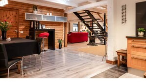 A spacious living area with a wooden floor, a dining table with chairs, a red sofa, and a staircase leading to another level.