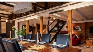 A dining area with a wooden table set for four, surrounded by black leather chairs. A staircase is visible in the background leading to an upper level.