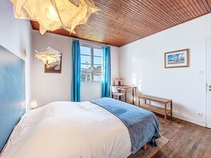Un dormitorio con cama, escritorio, silla, lámpara colgante, ventana con cortinas e imagen enmarcada en la pared.