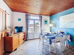 Un comedor con una mesa dispuesta para cuatro personas, un mueble de madera con un televisor y una ventana con cortinas.