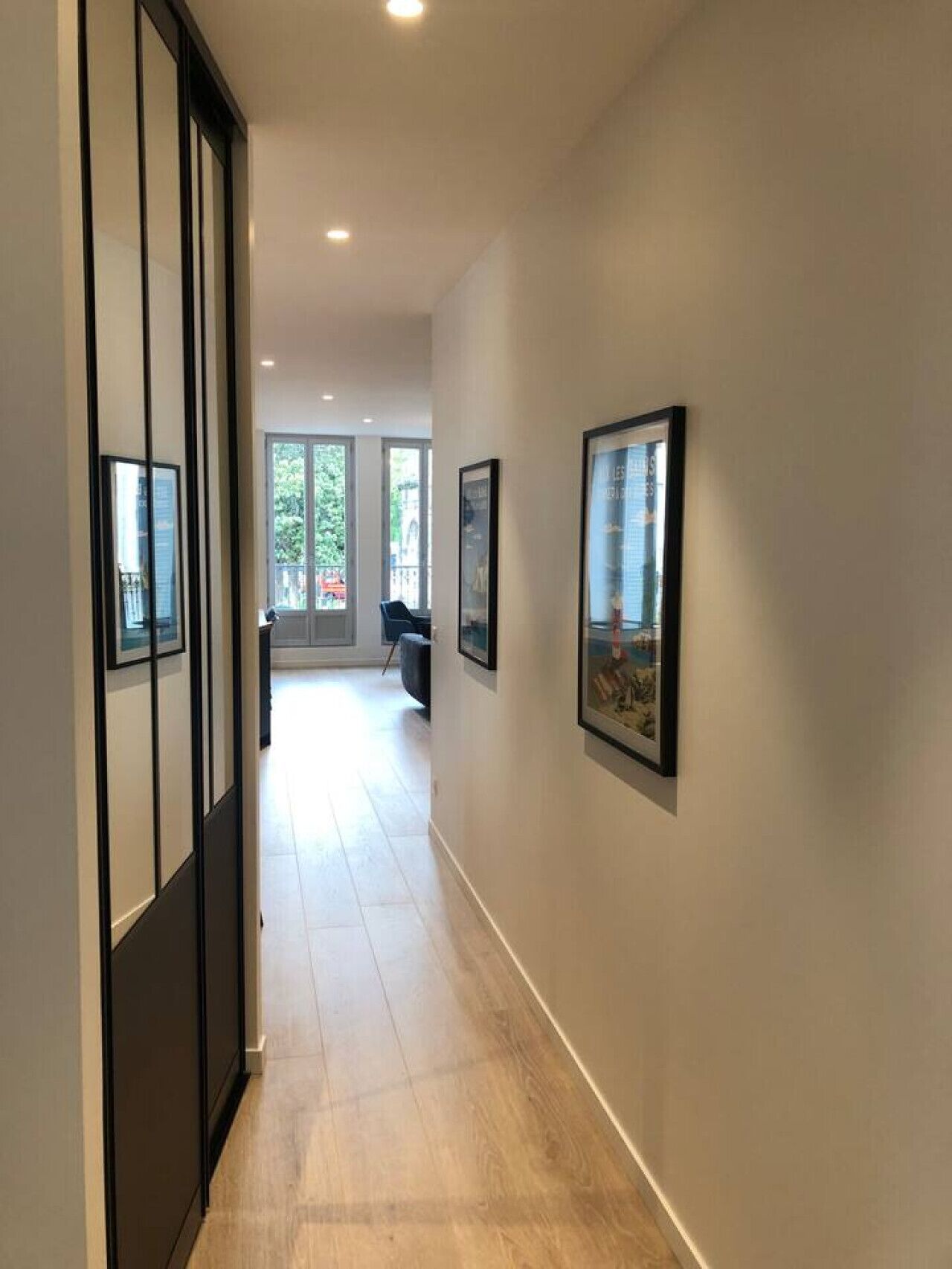 Een gang met inlijste foto’s aan de wanden, een houten vloer en uitzicht op een balkon met een stoel.