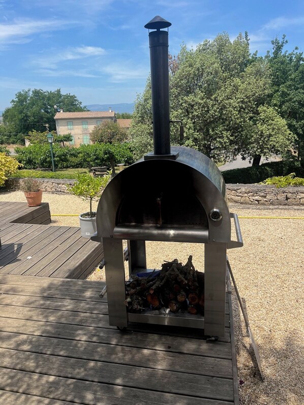 A wood-fired pizza oven on a wooden deck with a stone wall and potted plants in the background. - Lock view, newly renovated apartment on Canal Du Midi, near Carcassonne (Marseillette)
