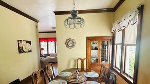 Un comedor con una mesa de madera, sillas, una araña y vistas al exterior a través de un ventanal.